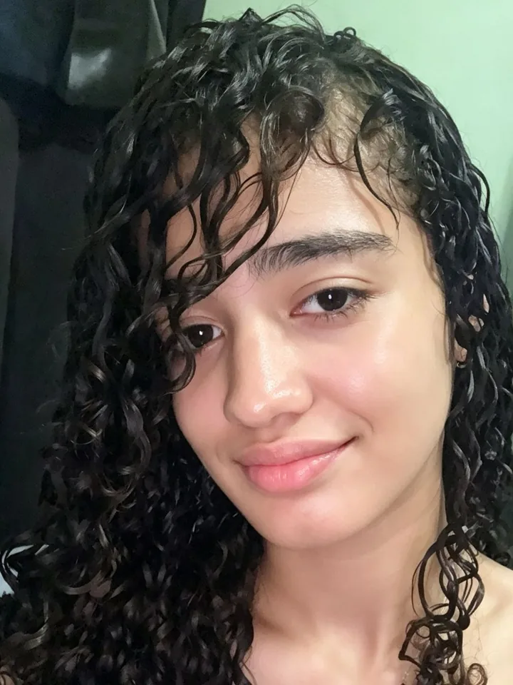 A woman with curly hair smiling at her camera, ready for a 1v1 video call